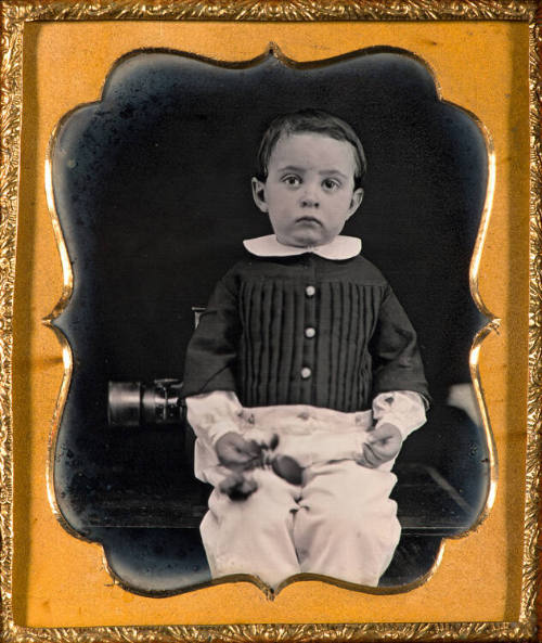 Boy leaning against daguerreian camera
