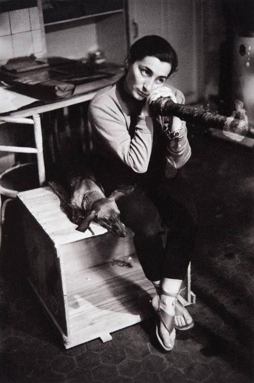 Jacqueline and Lump sit on an empty box in basement of villa, which Picasso converted into engraver's printing plant, while he etches the copper plates of the bullfight series