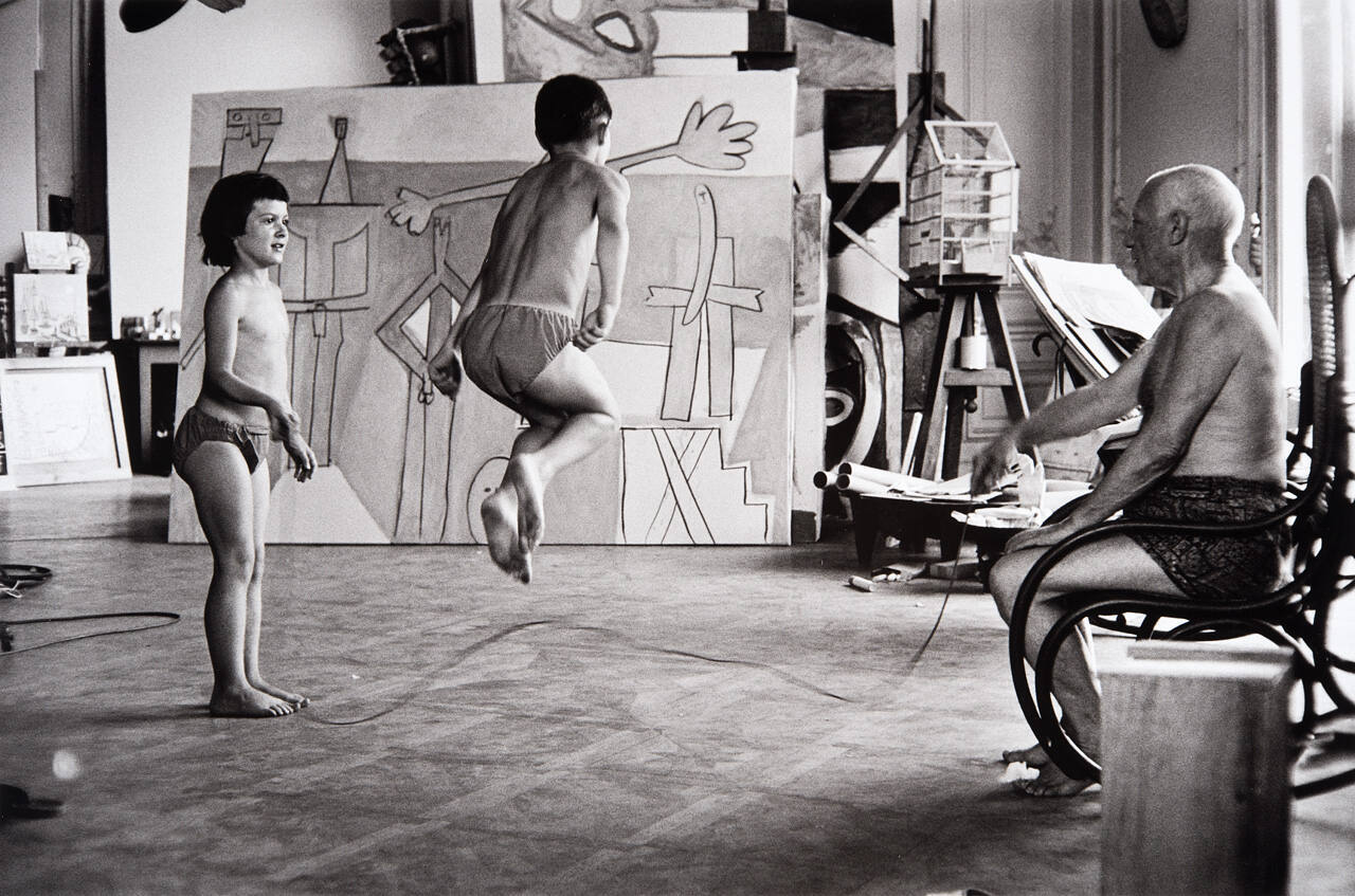 Paloma and Claude skipping rope in the studio, with Picasso holding one end of the rope. The new "La Garoupe" picture forms the backdrop.