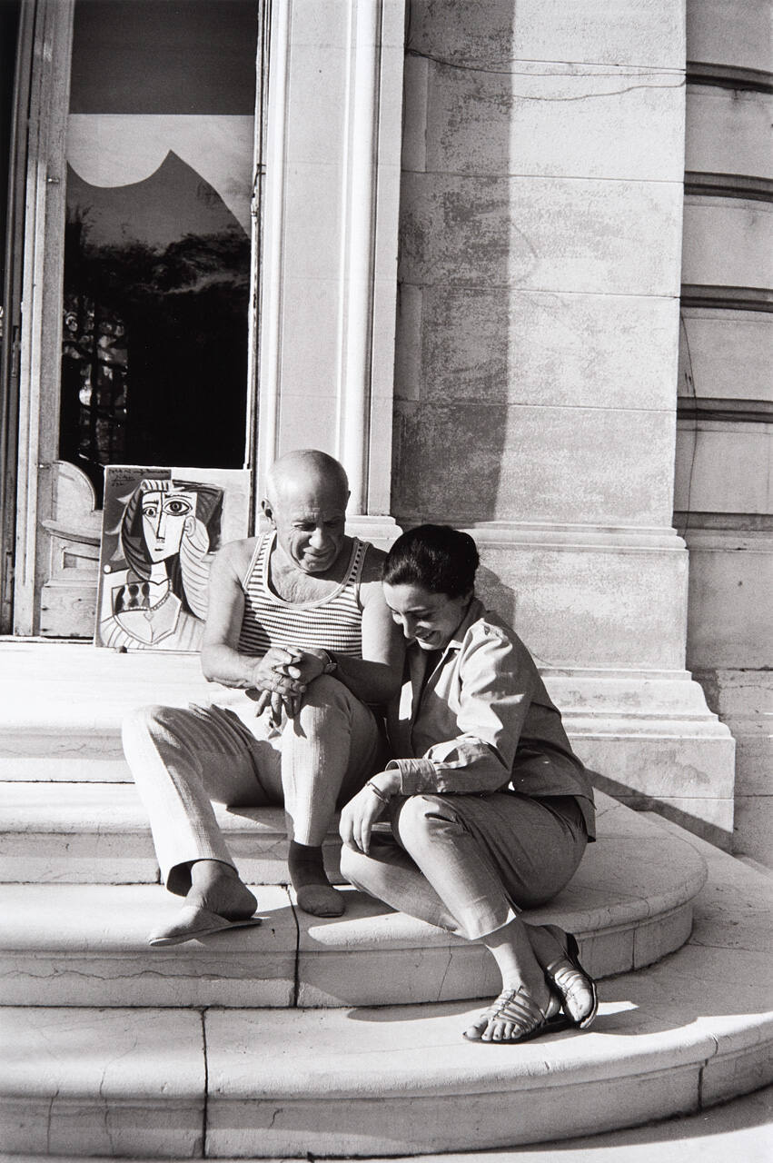 Picasso and Jacqueline sitting on the back steps where a portrait of her leans against the doorway, an inscription drying in the afternoon sun