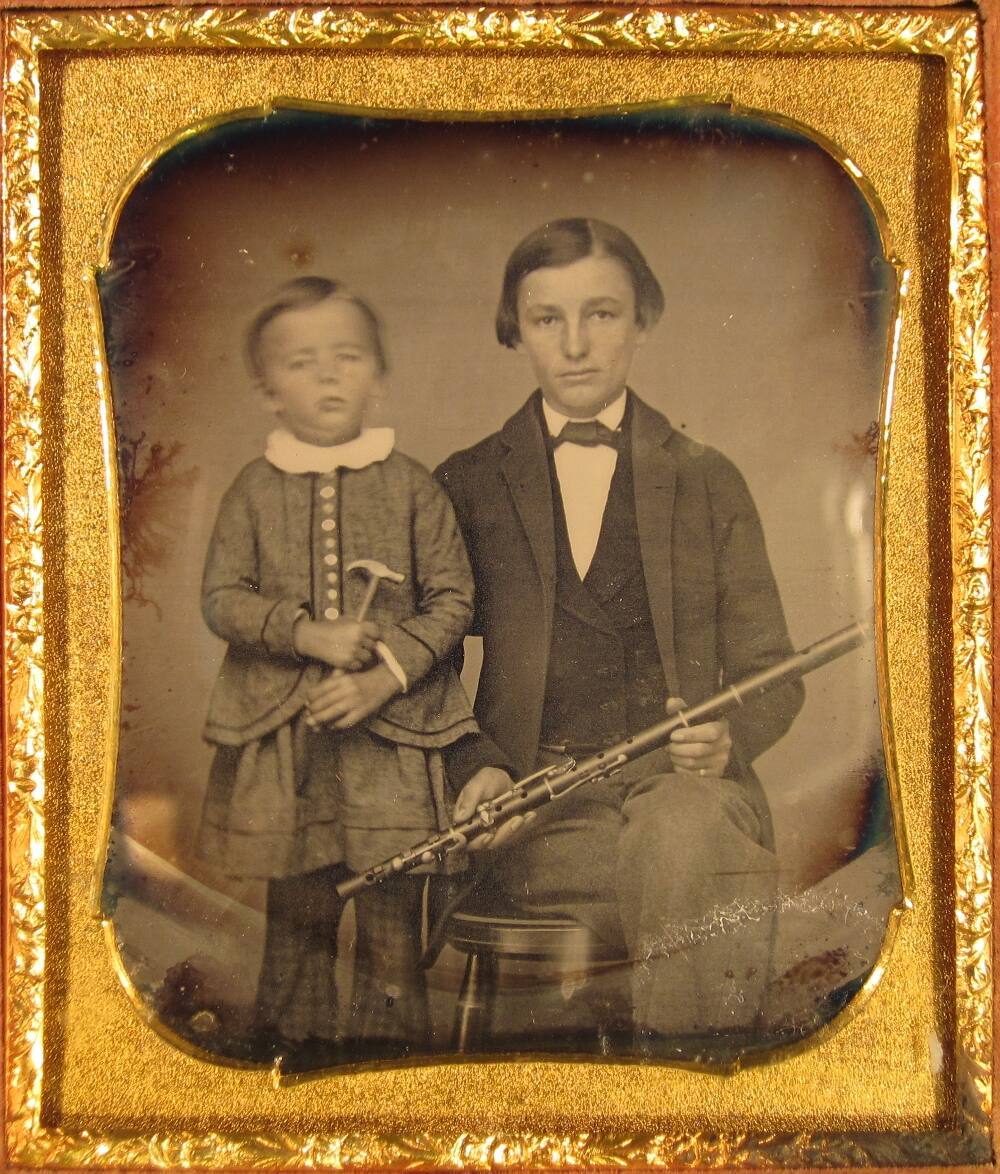 Young man holding flute, with young boy holding toy hammer