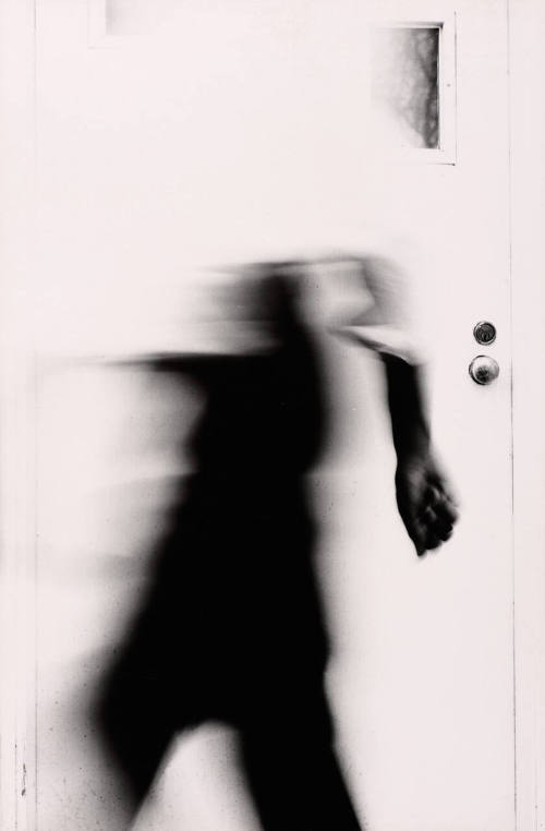 [Blurred figure in front of white door]