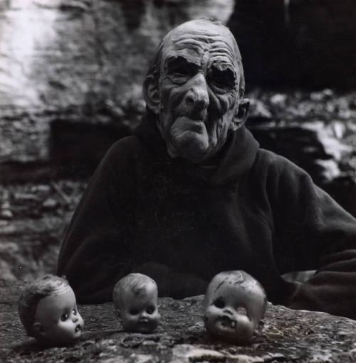 [Masked figure with three doll's heads]