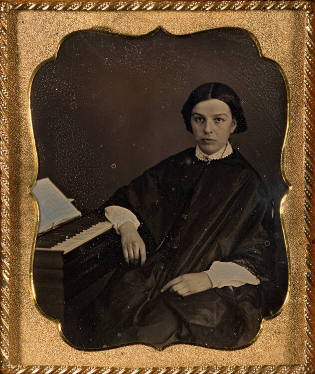 Woman in dark shawl, seated w/arm resting on keyboard