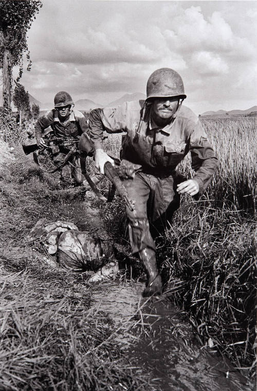 Two Marines, under enemy fire, run through a rice paddy in South Korea