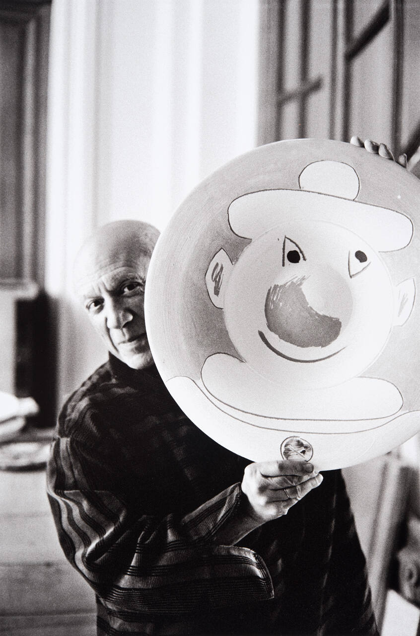 Picasso checks on plates after they have been fired, examining each to see how it turned out. Here he holds plate with clown face.